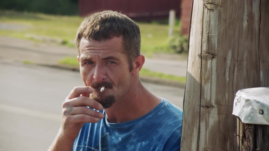 A man smokes a cigarette next to a telephone pole