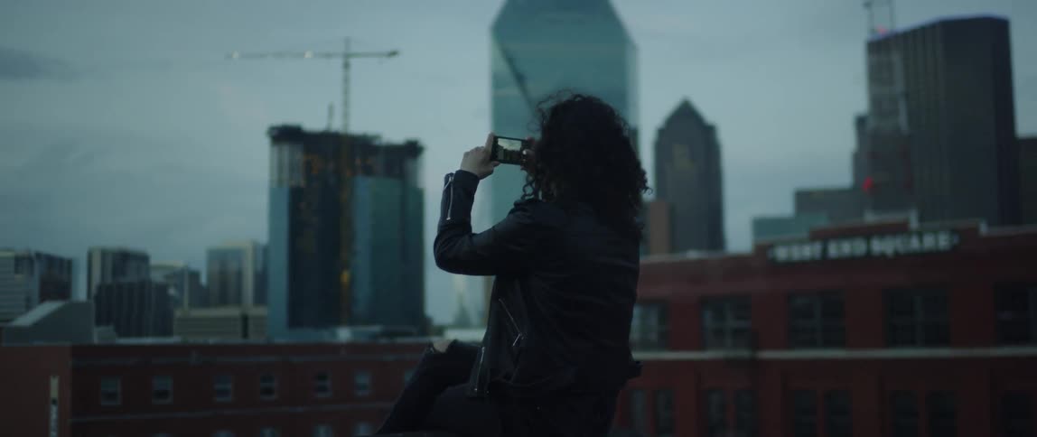 A woman sits on the roof taking pictures with her phone