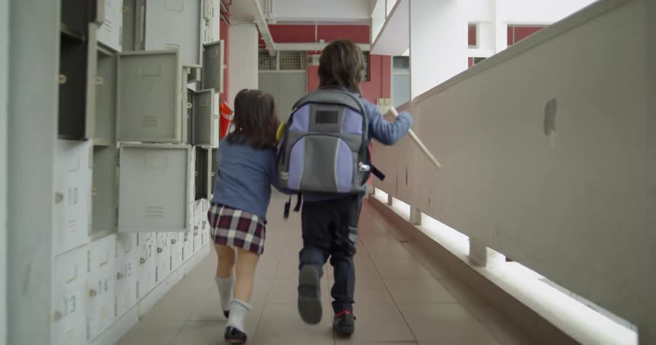 Two children are running through a school hallway together during the day