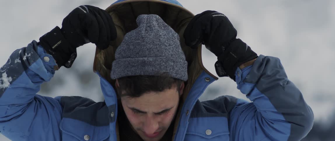 A man puts on a coat hood outside in the snow