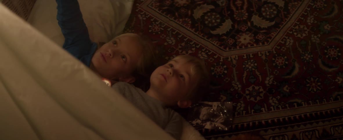 Two blonde children laying in bed shining flashlights at the ceiling, talking and laughing