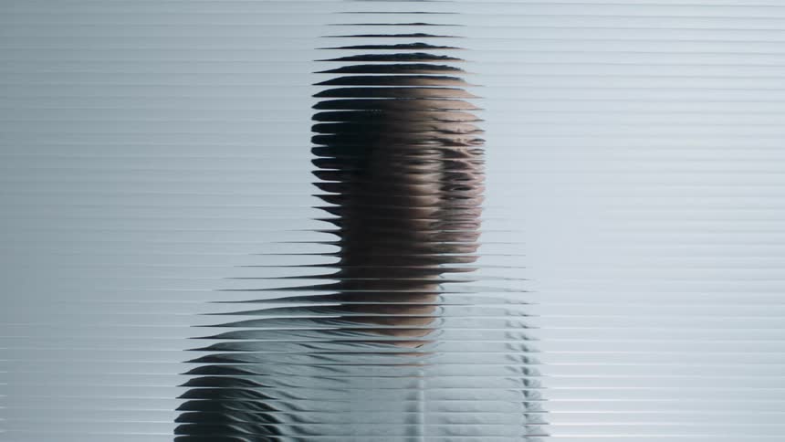A man stands behind a textured window