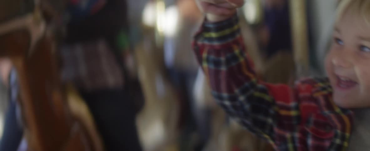 Blonde child sitting on a toy horse on a carrousel holding hands with his mother