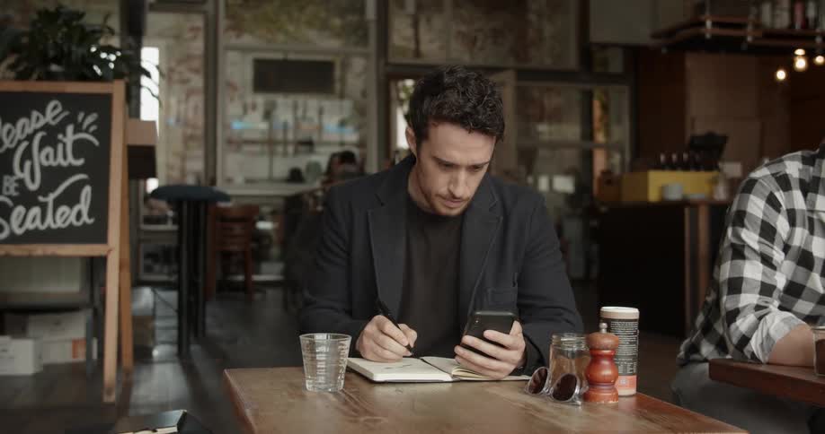 A man sits at the table in a restaurant writing
