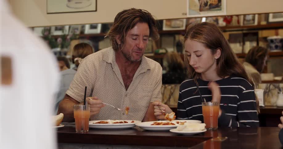 A man and his daughter are sharing a meal at a cafe during the day
