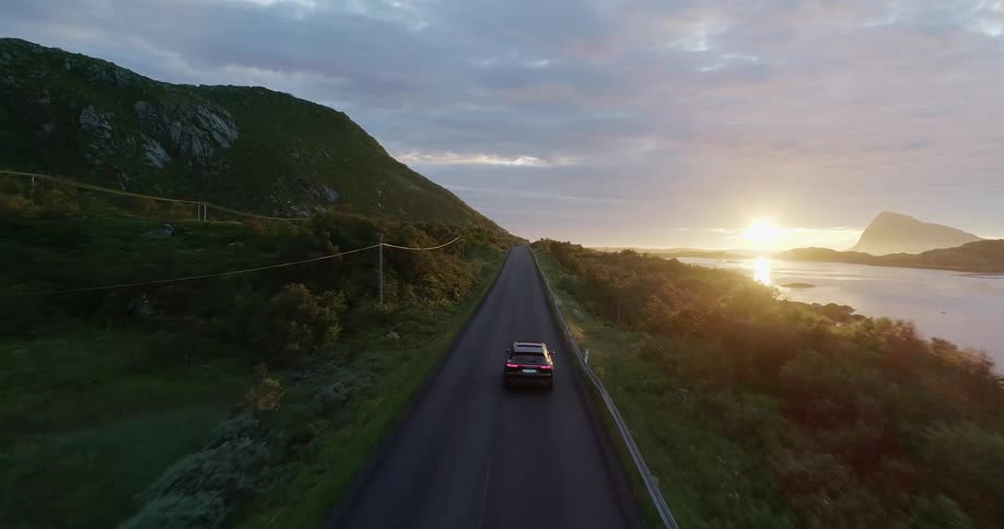 Car travels down a highway near a river under a cloudy sky