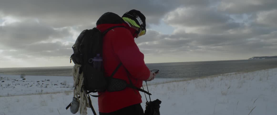 A hiker uses a piece of electronic equipment in the snow