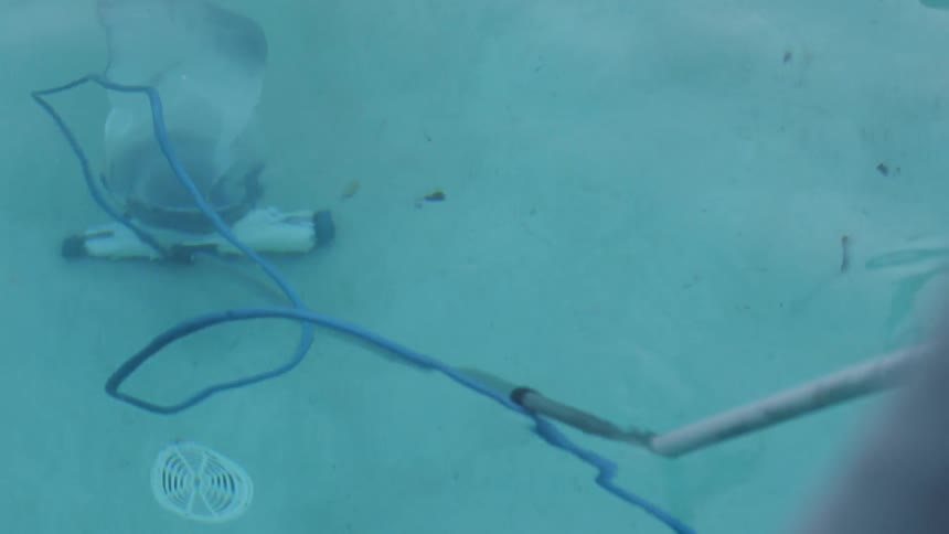 A person is using a vacuum to clean the bottom of the pool