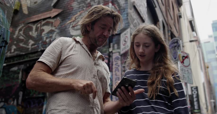 Man and teenage girl talk while looking at a smart phone in a city