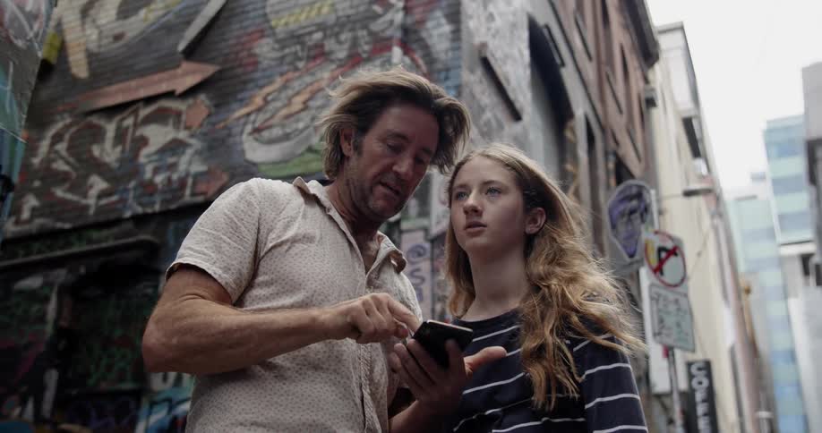 A man and teenage girl stand on a city sidewalk