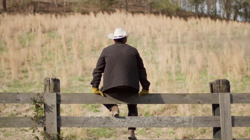 A man sits on a wooden fence