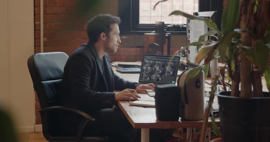 A man sits at a desk and works on a laptop and monitor