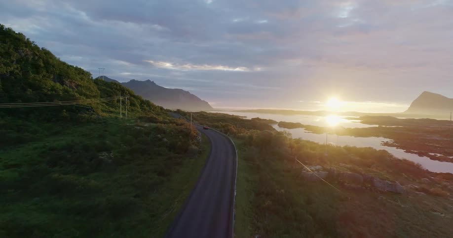 Car drives on a lakeside road at sunset