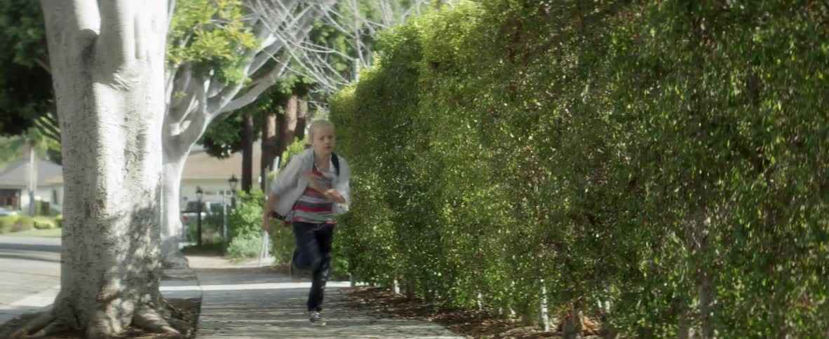 Child running down a hedge-lined sidewalk