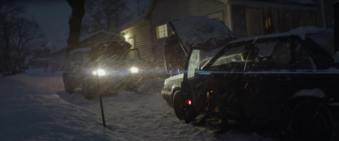 A car is given a battery jump in a snowstorm
