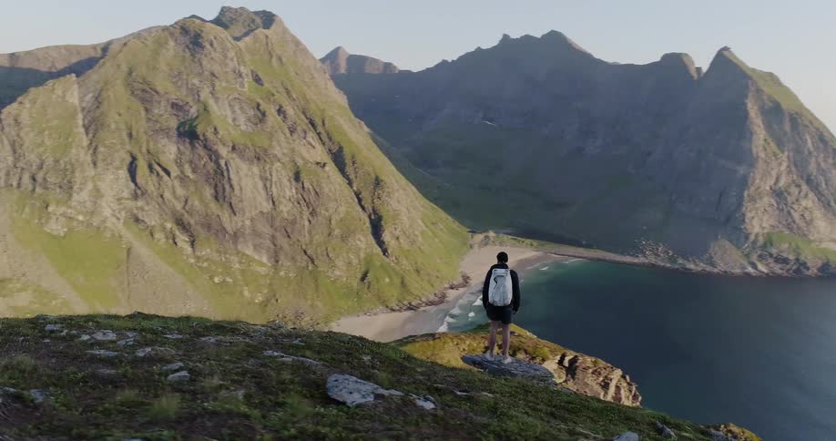 A person stands by a cliff near the shore