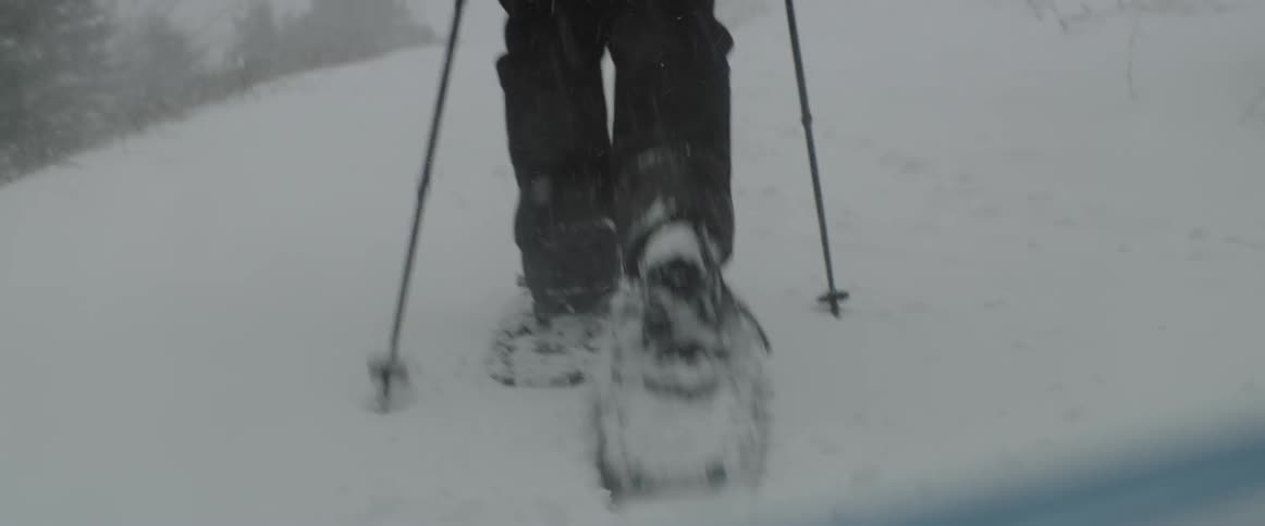 A person snowshoes up a slope while it is snowing