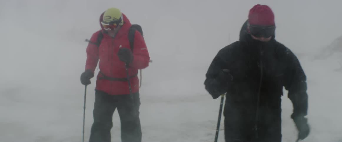Two people hiking outside in the blowing snow using long poles