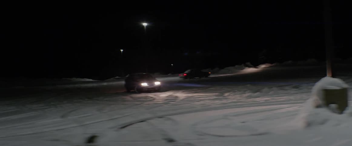 A vehicle is spinning out backwards in a vacant lot at night in winter