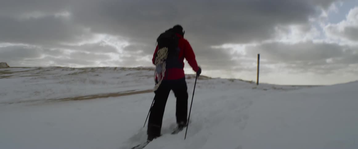 Man walking through snow with poles on a cloudy day