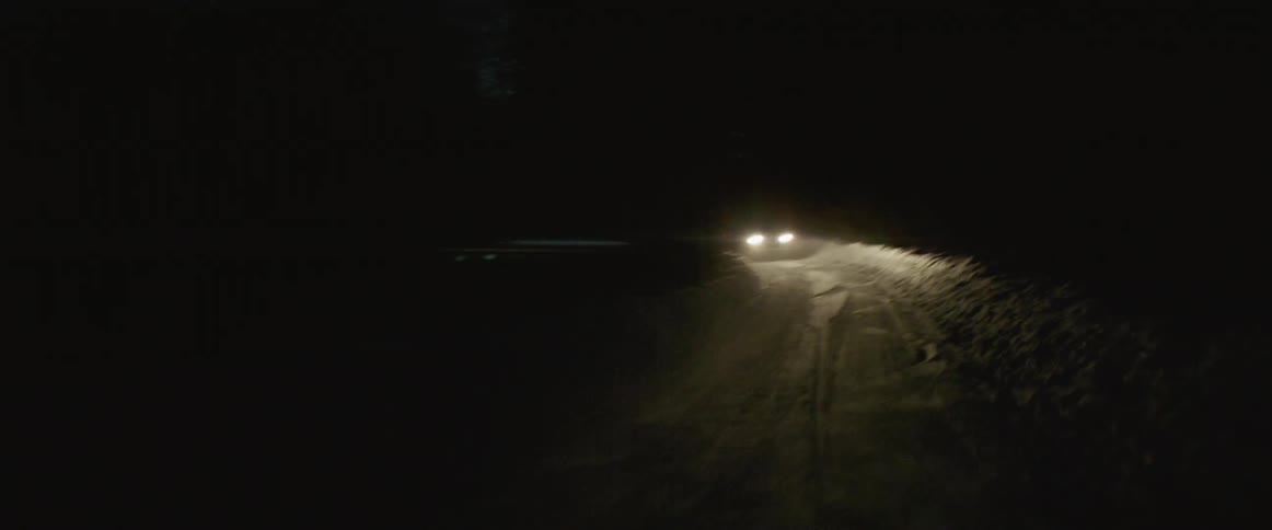 A car drives on a snowy road at night