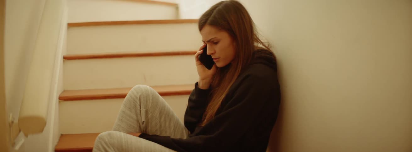 A woman sits on a staircase while using a phone