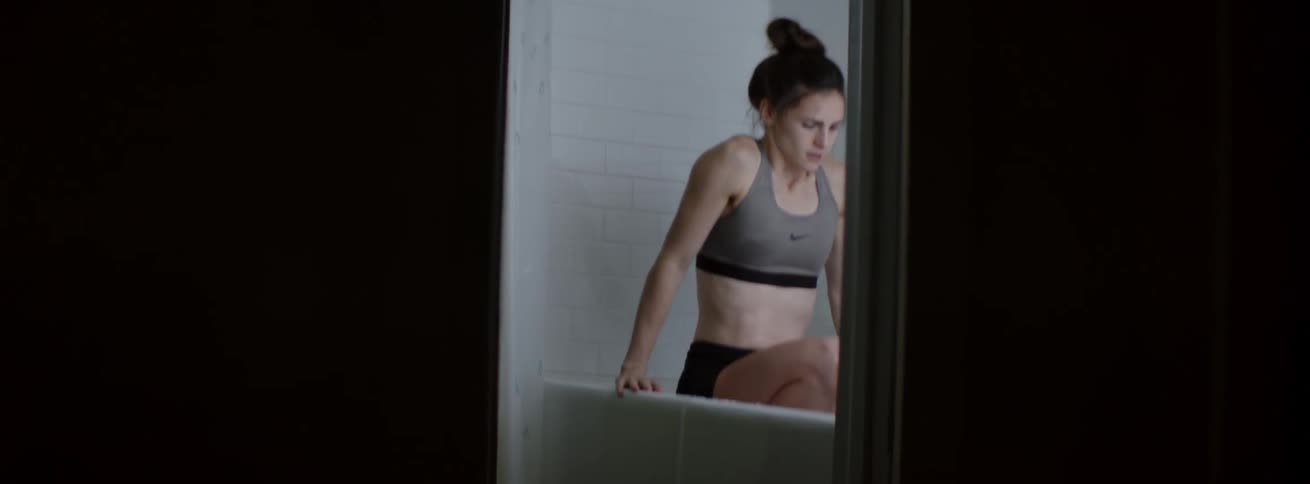 A woman in shorts and sports bra lowers herself into a bath