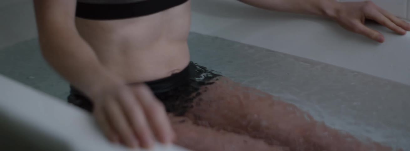 Woman sits in an ice bath while wearing a sports bra and underwear