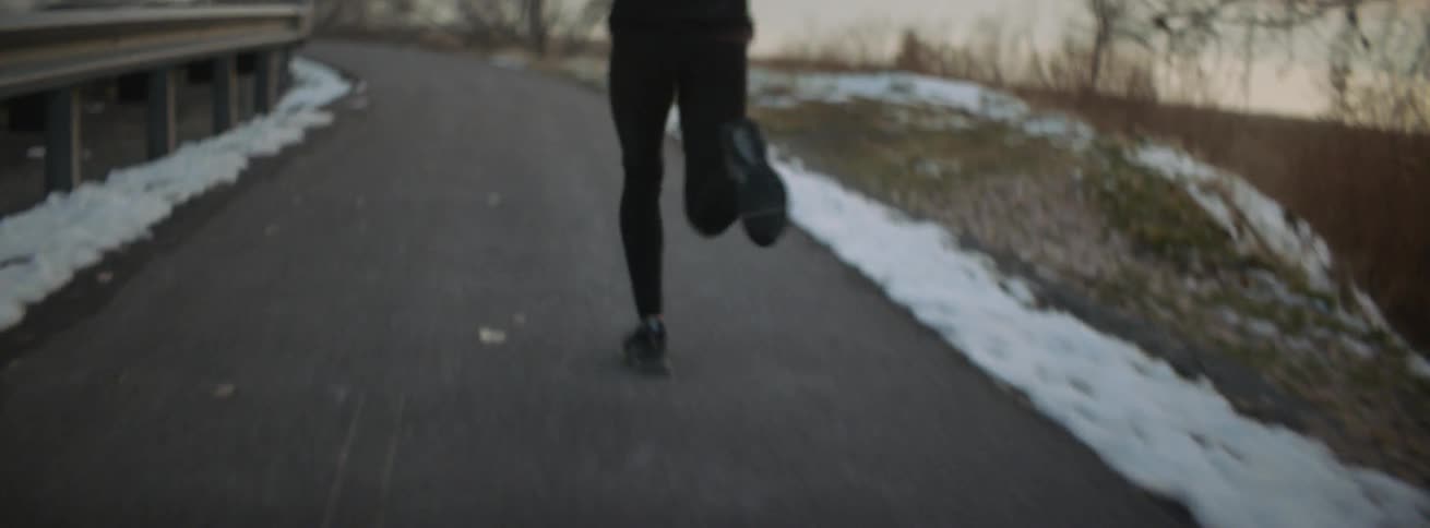 Woman runs down a paved trail near the snow