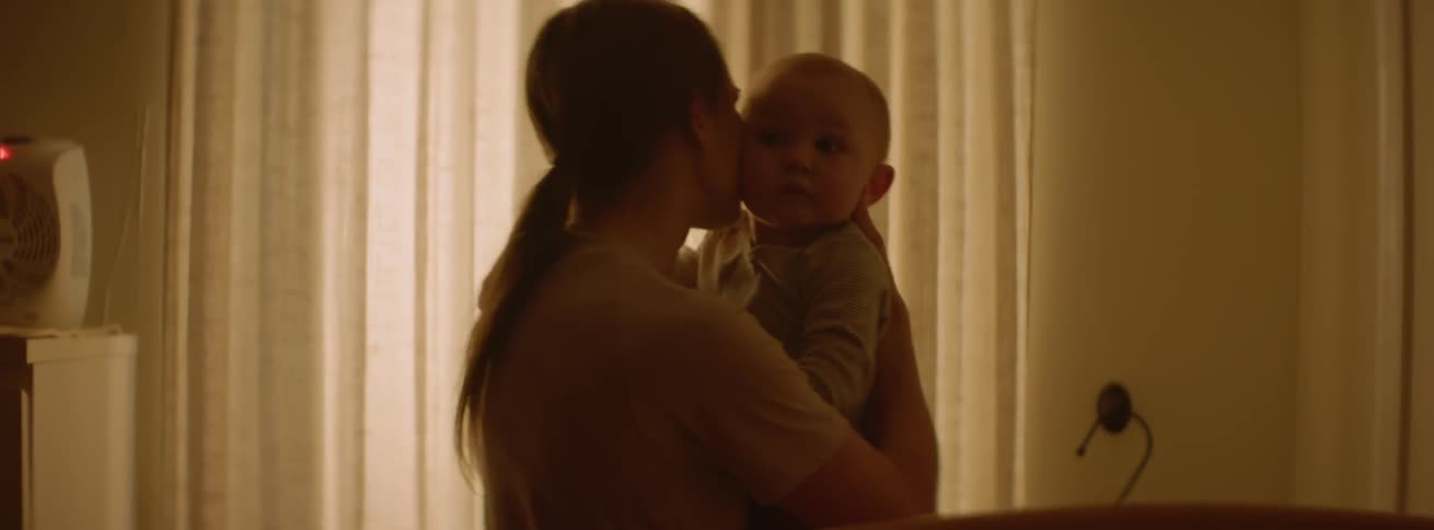 A woman is rocking and comforting her baby as she stands inside in daylight