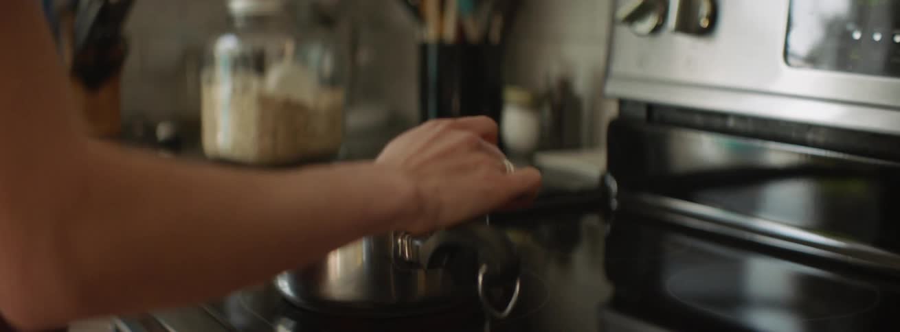 A woman holding a baby stirring food in a pot on a stove