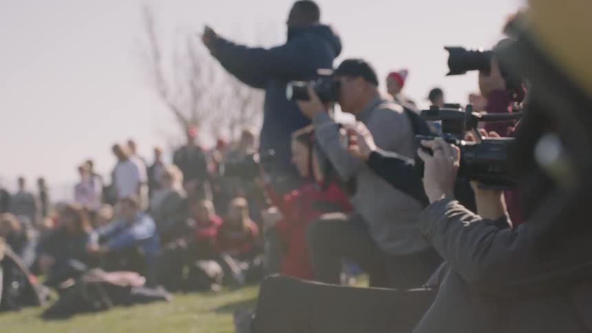 A crowd of photographers are taking pictures of an event outside in daylight