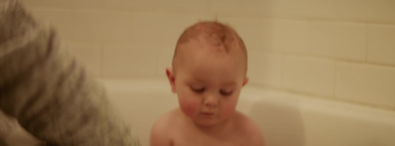 Baby splashes water as he sits in a bathtub