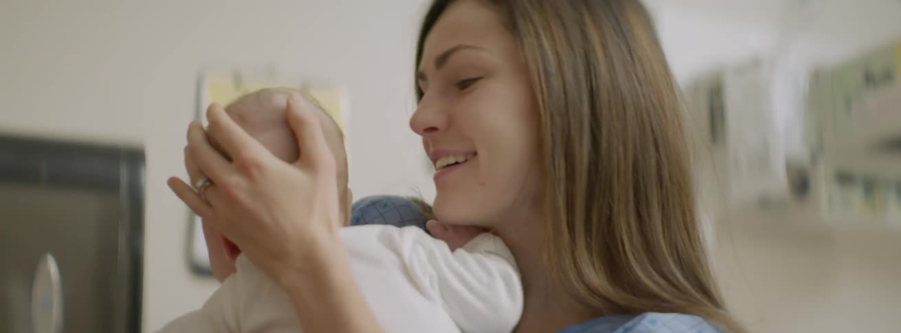 A woman wearing a hospital gown holds her baby and smiles