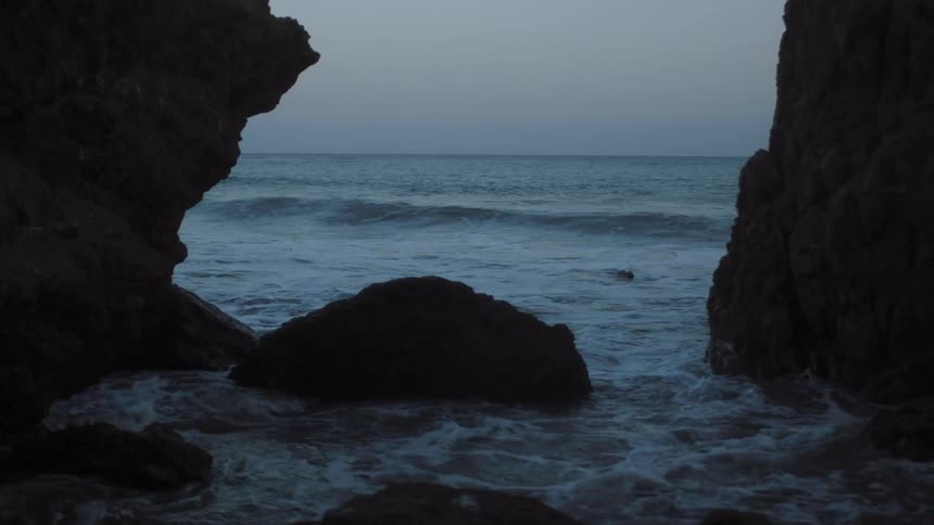 The waves crash against the dark rocks on the shore
