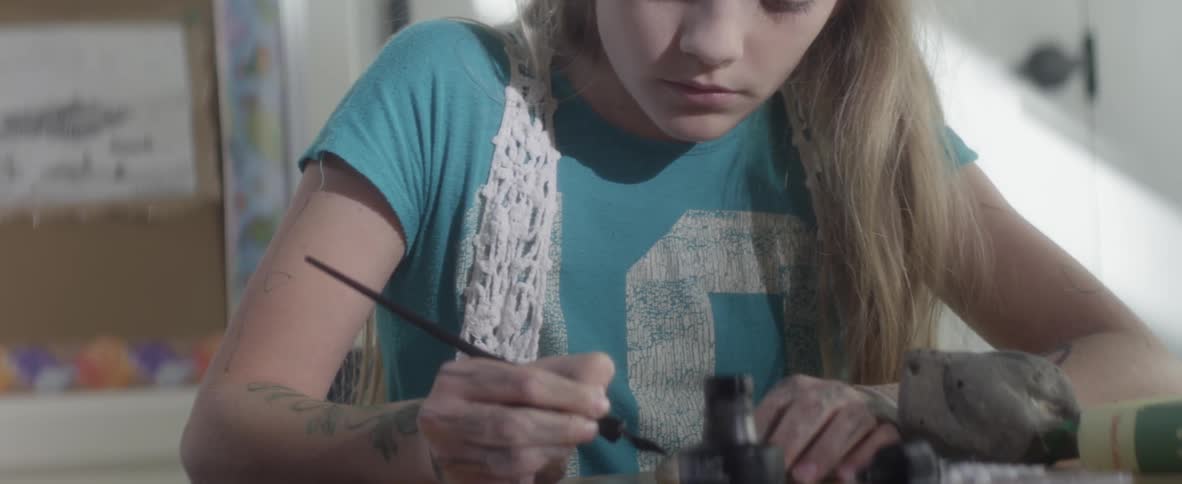 A girl sits painting designs onto small stones