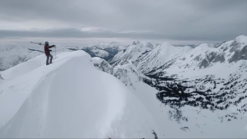 Person standing atop a snowy mountain on a cloudy day