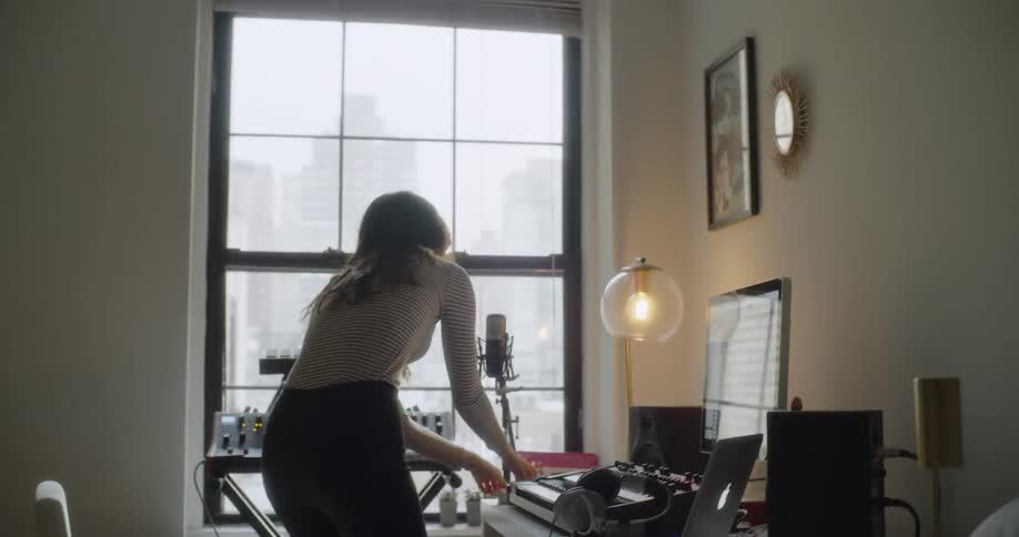 A woman sitting at a keyboard in her room during the day gets up and rushes away