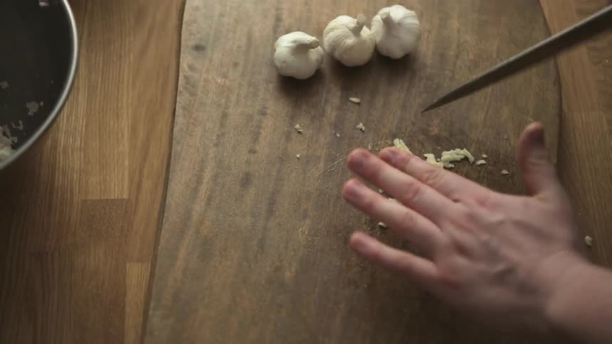 A person chopping garlic on a wooden table