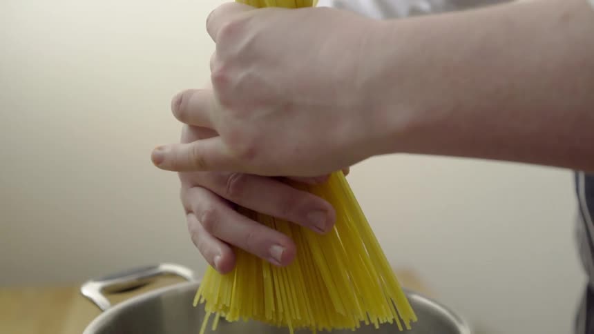 A person places spaghetti noodles into a pot