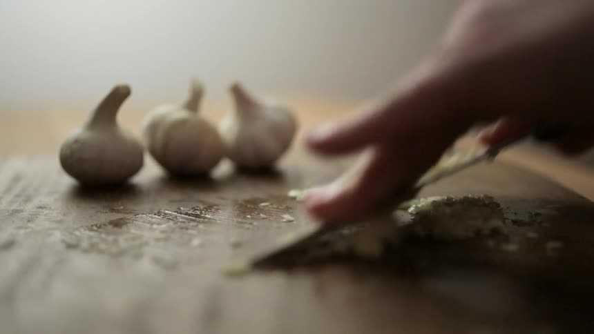 A person chops garlic on a wooden cutting board