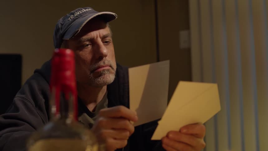 Man wearing a hat sits as he holds two photographs