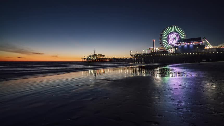 The lights on a ferris wheel are flashing as dusk settles in over a pier and beach