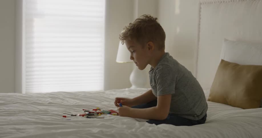 A boy jumps up on a bed to play with a pile of legos