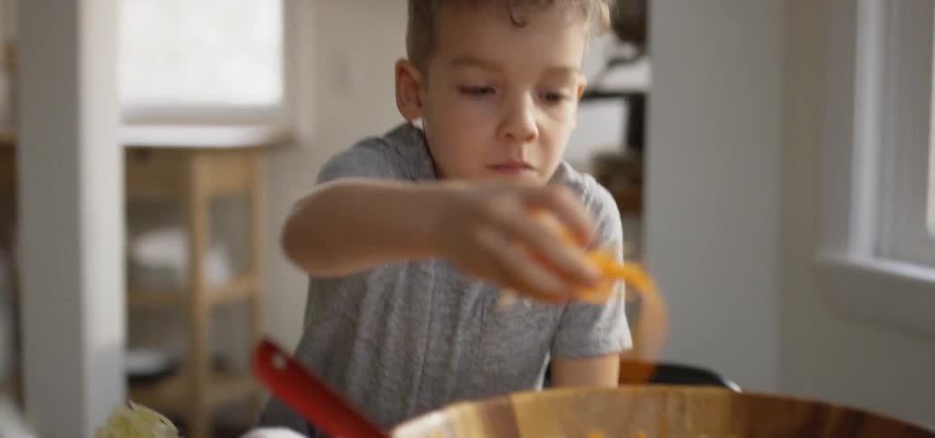 A young boy sprinkles cheese on a bowl of lettuce