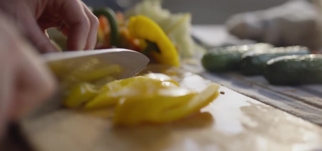 Person uses a large knife to chop banana peppers