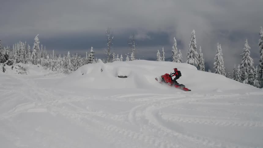 Snowmobile travels over a snowy hill under a dark sky