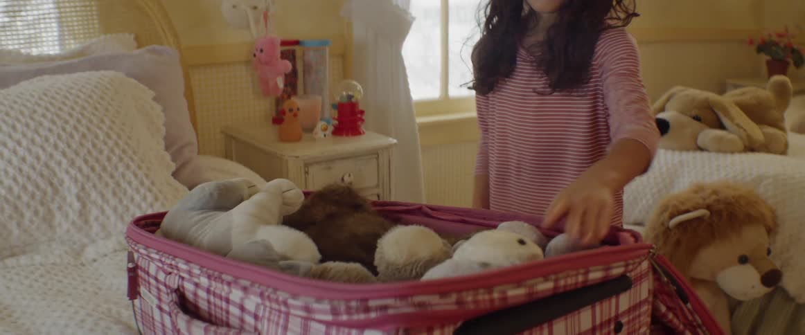 Girl packs stuffed animals in suitcase