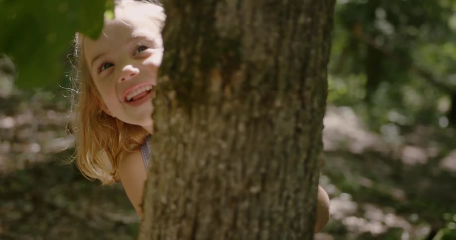 Child standing behind a tree smiles and looks out