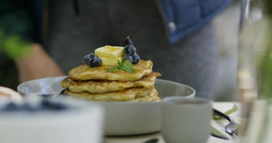 Syrup being poured on a stack of blueberry pancakes
